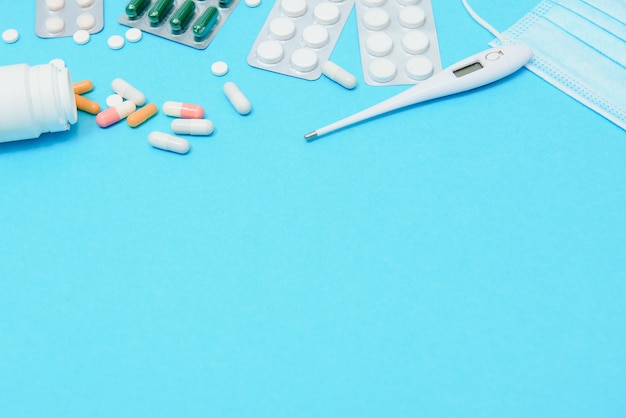 Sparse pillole bianche sul tavolo blu. Medicina, farmacia e concetto di assistenza sanitaria. Pillole di sfondo blu bianco con uno statoscopio medico, vista dall'alto.