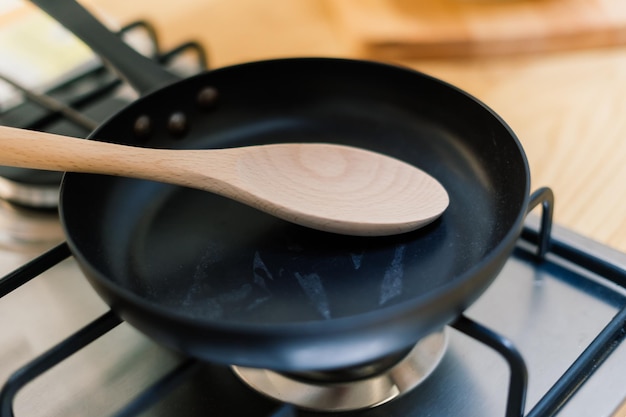 Spatola in padella con rivestimento in teflon sul fornello a gas contro il cucchiaio appeso nella piccola cucina