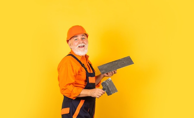 Spatola per cazzuola in gesso su cartongesso giallo. Stuccatore in intonacatura uniforme di lavoro. uomo con spatola. processo di applicazione dello strato di mastice. Strumenti di intonacatura per intonaco.