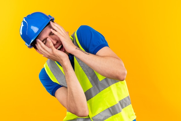 Spaventato con gli occhi chiusi, il giovane costruttore in uniforme ha il viso coperto con le mani
