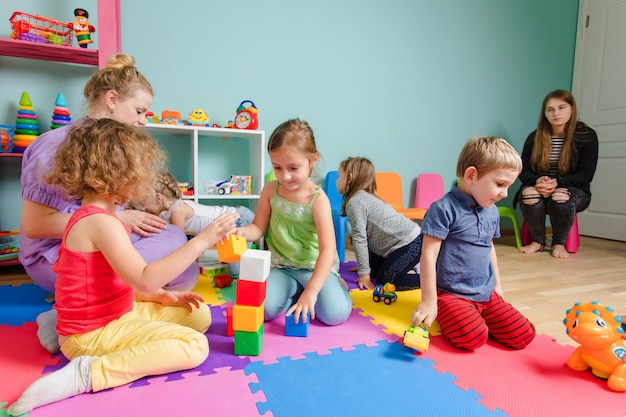 Spazio di sicurezza per lo sviluppo dei bambini Ragazzi e ragazze adorabili che costruiscono una torre di mattoni colorati nell'asilo Sala giochi con vari giocattoli educativi