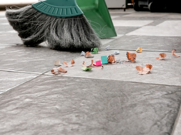 Spazzare ritagli di carta e polvere sui pavimenti piastrellati con una scopa e una paletta di plastica.