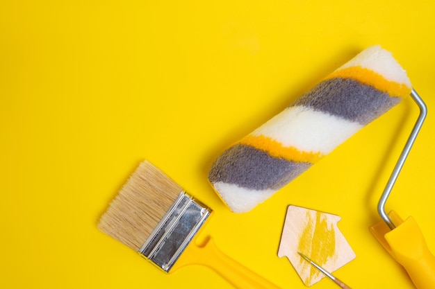 Spazzola di protezione del rullo di vernice per dipingere pareti su sfondo giallo e figurine di una casaConcetto di ristrutturazione domestica