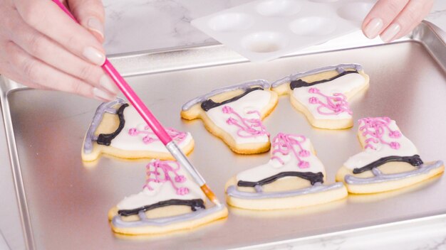 Spazzolare i glitter commestibili sui biscotti di zucchero da pattinaggio artistico ghiacciati.