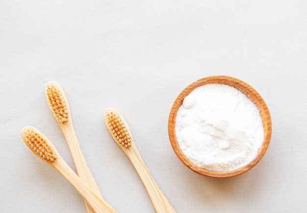 Spazzolini da denti amichevoli di legno di bambù di eco, bicarbonato di sodio su fondo bianco. Cure dentistiche e concetto di rifiuti zero