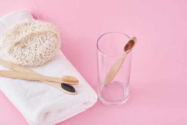 Spazzolini da denti ecologici in legno di bambù, spugna e asciugamano bianco su sfondo rosa