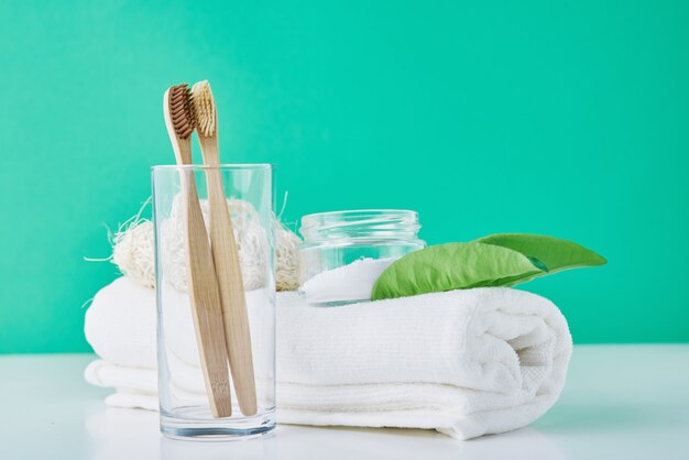 Spazzolini da denti in legno di bambù in vetro, bicarbonato di sodio e asciugamano su un verde. Concetto di igiene personale