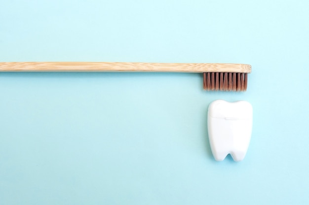 Spazzolino da denti di bambù e filo interdentale bianco a forma di dente bianco su sfondo blu.