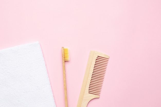 Spazzolino da denti di legno di Eco, pettine e asciugamano di bagno bianco sul rosa