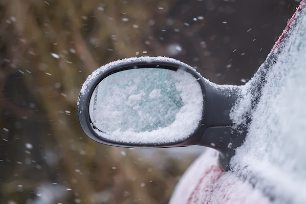 Specchietto retrovisore auto coperto di neve fresca e bagnata.