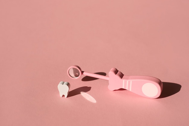 Specchio di ispezione dentale giocattolo per la chiusura dei denti su sfondo rosa con ombra profonda