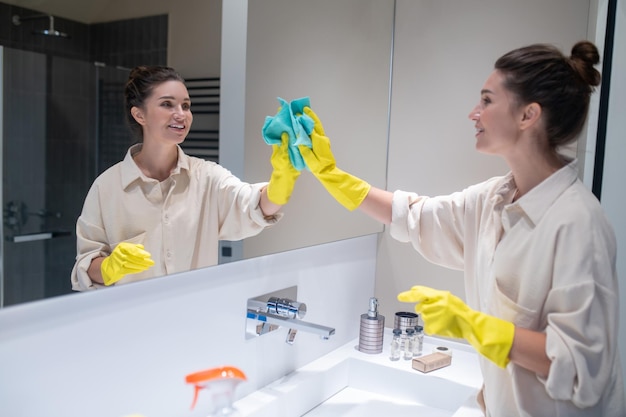 Specchio di pulizia della giovane donna sveglia in bagno