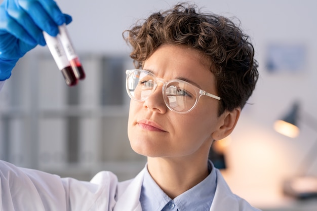 Specialista di laboratorio concentrato tenendo test di laboratorio di campioni di sangue e confrontandolo