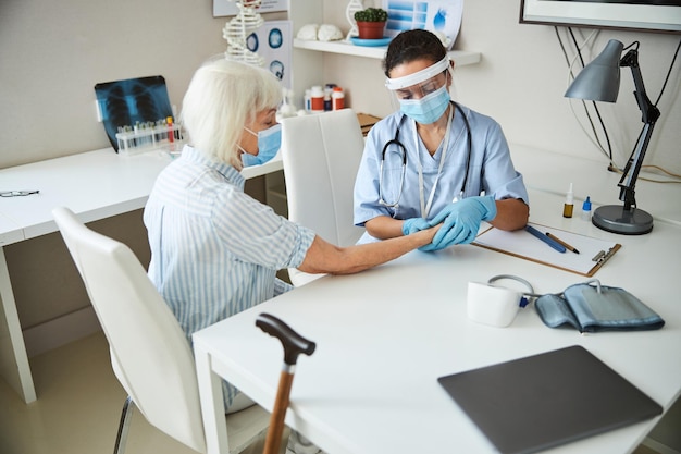 Specialista medico attento che tocca il polso della donna invecchiata con due pollici