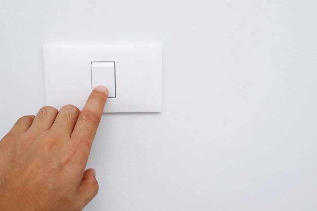 Spegni la luce vicino al dito la mano dell'uomo sta chiudendo l'interruttore di alimentazione con il muro a casa per risparmiare energia e ridurre il riscaldamento globale