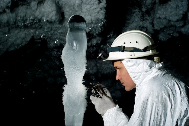 Speleologo in una grotta esamina una gigantesca stalagmite di ghiaccio ricoperta di brina