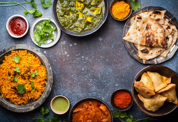 Spese generali di piatti e antipasti tradizionali indiani: pollo al curry, pilaf, pane naan, samosa, paneer, chutney su fondo rustico. Tavolo con scelta di cibo della cucina indiana, spazio per il testo