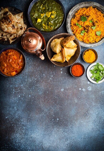 Spese generali di piatti e antipasti tradizionali indiani: pollo al curry, pilaf, pane naan, samosa, paneer, chutney su fondo rustico. Tavolo con scelta di cibo della cucina indiana, spazio per il testo