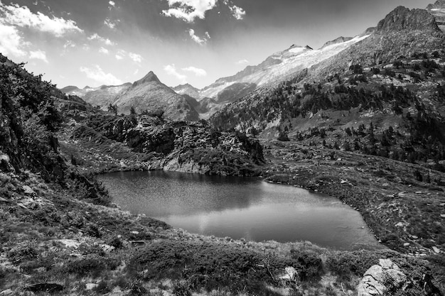 Spettacolare paesaggio meraviglioso e suggestivo di un lago dei Pirenei circondato da montagne e vette innevate di Benasque Bianco e nero Monocromatico