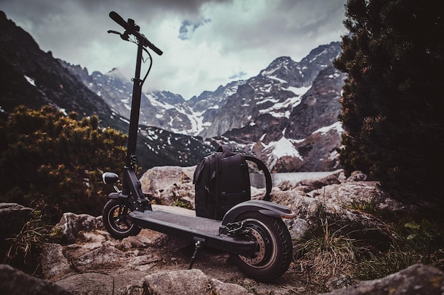 Spettacolare vista su montagne, pini e nuvole basse e cupe con zaino e scooter nella parte anteriore.