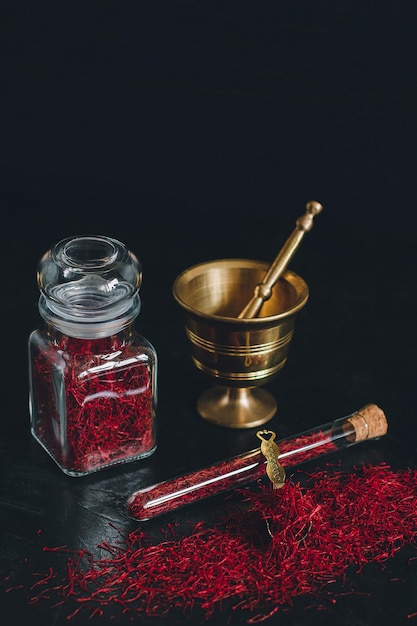 Spezia di zafferano essiccata rossa organica cruda su fondo di legno in mortaio d'ottone del metallo dell'annata con il vaso e il tubo di vetro del pestello