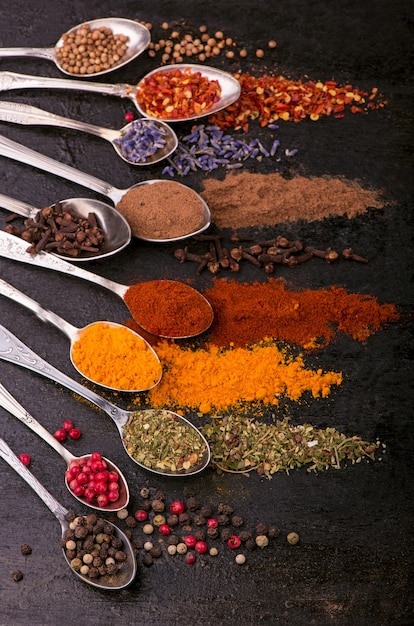 Spezie secche - pepe, curcuma, paprika, anice, lavanda, adjika, coriandolo in cucchiai vecchi su sfondo nero