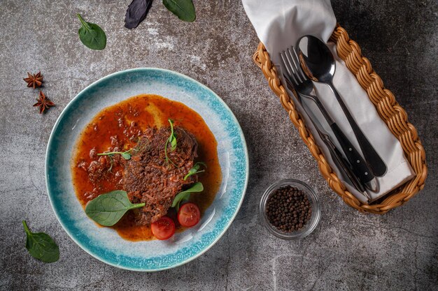 Spezzatino di manzo con brodo ed erbe aromatiche in un piatto blu con spezie e pepe nero su un tavolo di pietra grigia