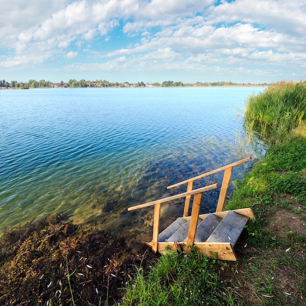 Spiaggia calma del lago d'estate con ripidi di legno all'acqua