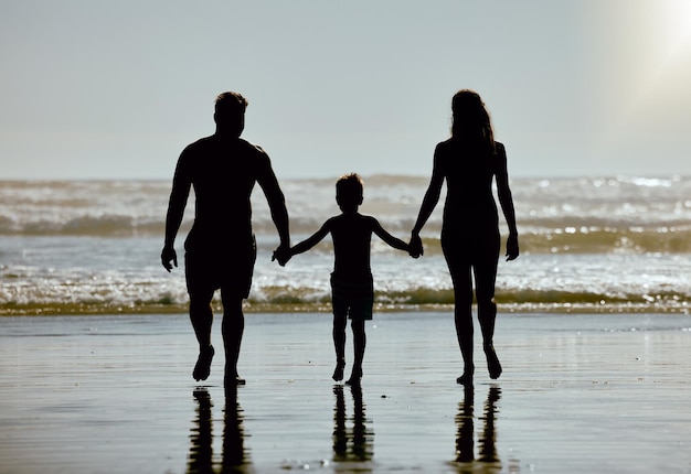 Spiaggia che si tiene per mano e famiglia con la silhouette di madre e padre del bambino che cammina nell'acqua dell'oceano sul mockup del cielo per le vacanze estive e i genitori ombra a sostegno dell'amore e della cura del bambino via mare