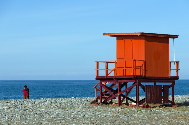 Spiaggia del mare con la torre del bagnino e una coppia vicino all'acqua.