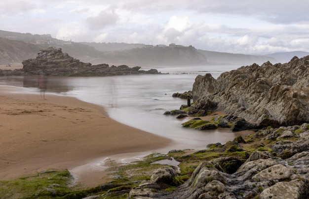 SPIAGGIA DEL NORD CON ONDE E ROCCE SOTTO CIELI NUVOLI DI PRIMAVERA