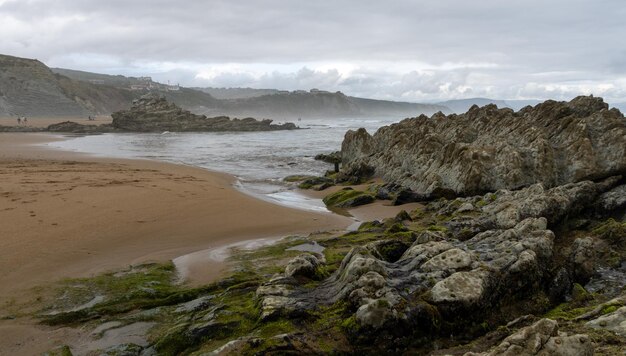 SPIAGGIA DEL NORD CON ONDE E ROCCE SOTTO CIELI NUVOLI DI PRIMAVERA