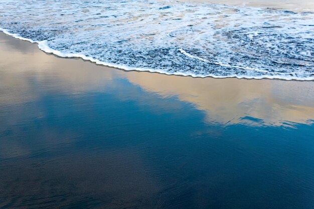 Spiaggia dell'oceano con sabbia vulcanica nera, il cielo si riflette nell'onda rovesciata del surf