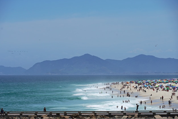 Spiaggia di Barra da Tijuca in una giornata di sole con persone che si godono la sabbia e il mare. Vista della diga foranea, del canale Barra e della Praia dos Amores. Rio de Janeiro, RJ, Brasile. febbraio 2021.