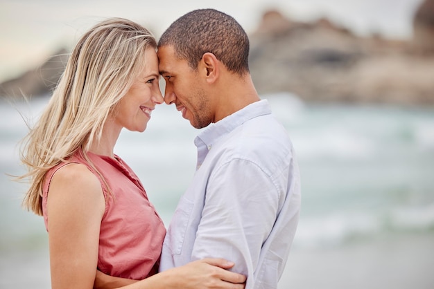 Spiaggia di coppia interrazziale e legame d'amore con la fronte insieme in sicurezza o sicurezza di fiducia Sorriso felice o latino uomo e donna in abbraccio dall'oceano o dall'acqua di mare nell'ambiente naturale per la data della luna di miele