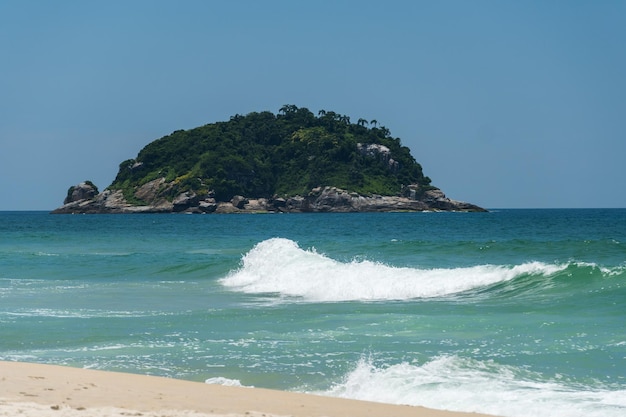 Spiaggia di Grumari vicino a Barra da Tijuca a Rio de Janeiro, Brasile. Giornata di sole con cielo azzurro, acqua limpida e piccole onde. Colline e natura intorno.