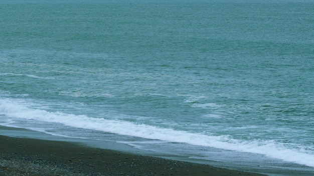 Spiaggia di pietra di piccoli ciottoli lavata da piccole onde schiumose acqua limpida dal mare ancora