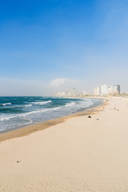 Spiaggia di sabbia con acqua limpida e grandi onde nel mare in una giornata di sole con i grattacieli della metropoli sul.