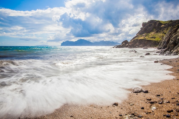 Spiaggia di sabbia con montagne sullo sfondo. Le montagne sono coperte di erba e hanno scogliere a picco sul mare. Il cielo è nuvoloso