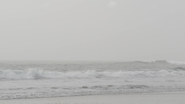 Spiaggia di sabbia nebbiosa, Encinitas California USA. Costa dell'Oceano Pacifico, fitta nebbia brume, riva del mare vuota. Costa vicino a Los Angeles, foschia lattiginosa di smog. Tempo cupo sul litorale. Onda d'acqua monocromatica grigia