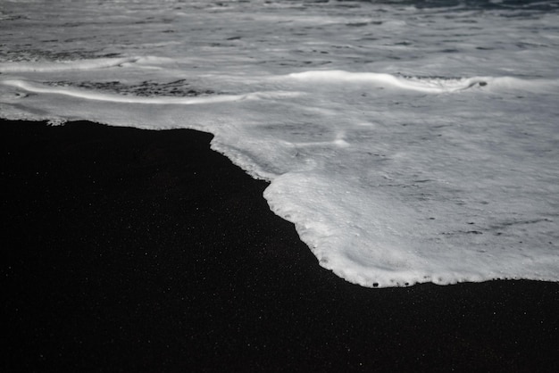 Spiaggia di sabbia nera per lo più sfocata con schiuma bianca delle onde del mare Sfondo bianco e nero con spazio di copia Foto di una spiaggia nera esotica Sabbia vulcanica scura e onde dell'oceano bianco