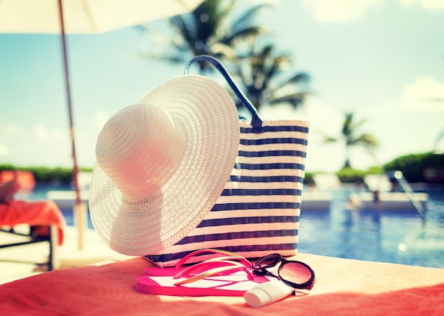 spiaggia, estate e vacanze e concetto - primo piano di cappello, borsa, crema solare e occhiali da sole in piscina