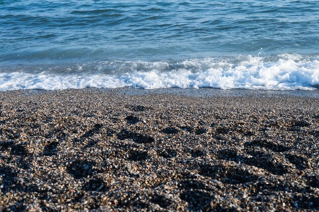 Spiaggia ghiaiosa con surf che si infrange sullo sfondo.