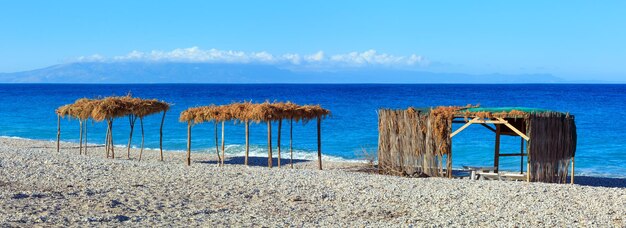 Spiaggia mattutina estiva con lettini, tettoie e ciottoli bianchi (Borsh, Albania). Panorama a punto due scatti.