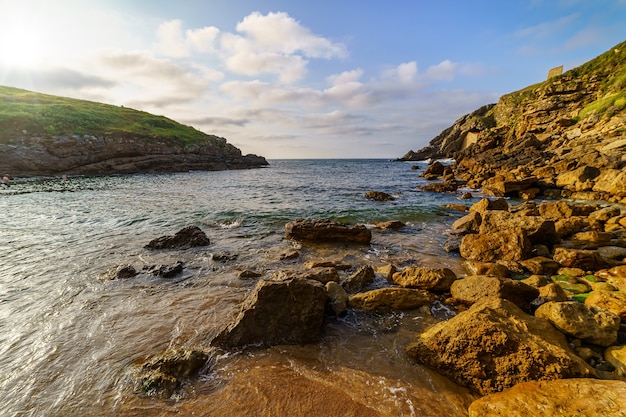 Spiaggia rocciosa in acqua limpida e scorci del sole che tramonta dietro la montagna Santander