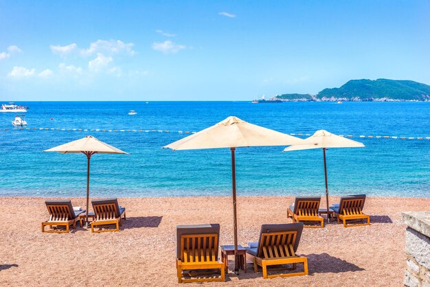 Spiaggia sabbiosa a Sveti Stefan con chaise-longue e ombrelloni al giorno d'estate, Montenegro