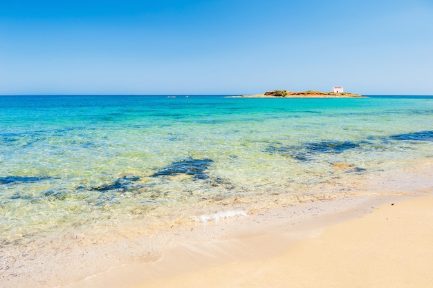 Spiaggia selvaggia con acqua turchese e isola con piccola cappella. Isola di Creta, Grecia