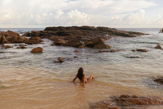 Spiaggia tropicale rocciosa con donna abbronzata in bikini durante le vacanze estive del fine settimana