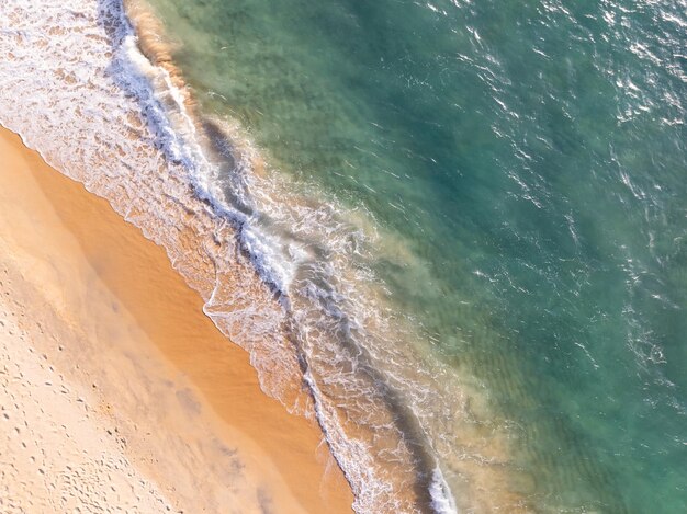 Spiaggia vista dall'alto con onde che si infrangono sulla riva sabbiosa. Bellissime onde della superficie del mare sullo sfondo del paesaggio marino estivo. Incredibile sfondo colorato di acqua della spiaggia
