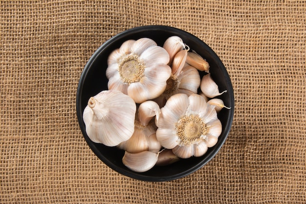 Spicchi d'aglio e lampadina in ciotola nera su iuta e sfondo scuro.